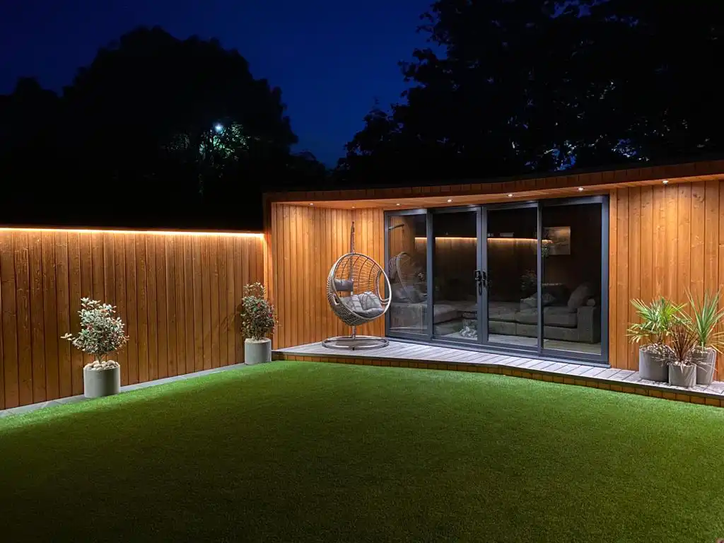 The front entrance of a wooden garden room with a hanging egg chair and plants next to the door